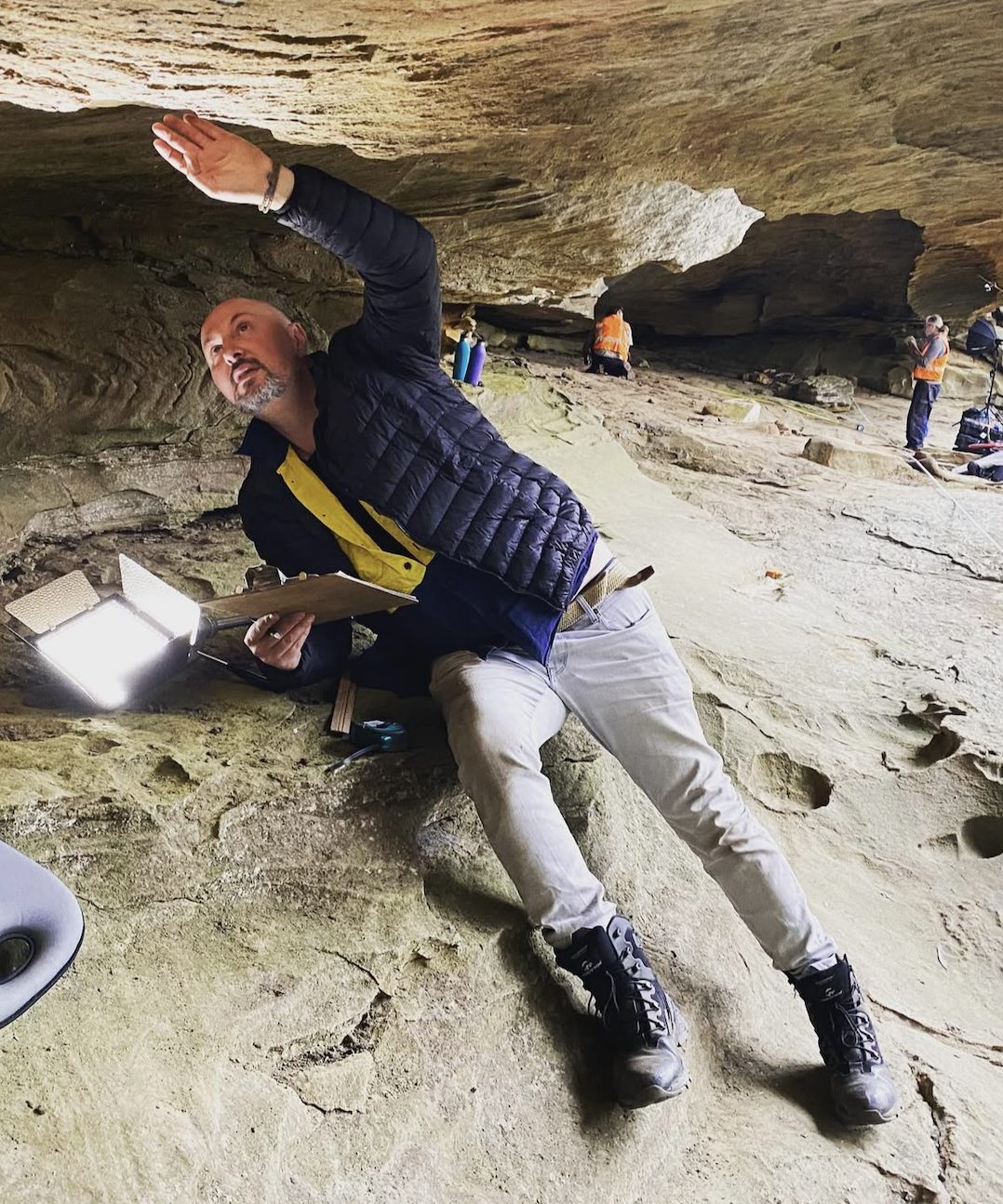 An archaeologist recording a rock shelter surface with lighting and field notes
